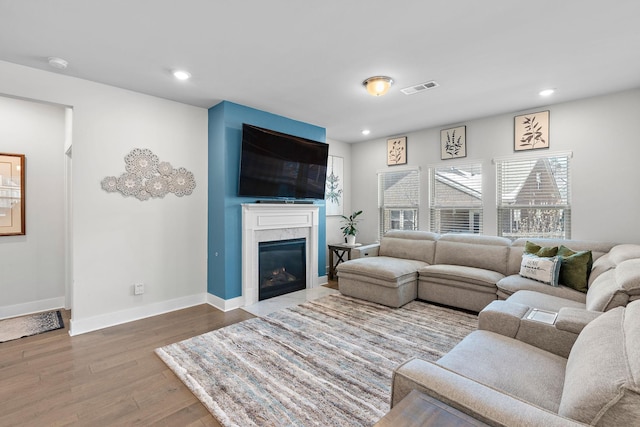 living room with baseboards, visible vents, a fireplace with flush hearth, wood finished floors, and recessed lighting