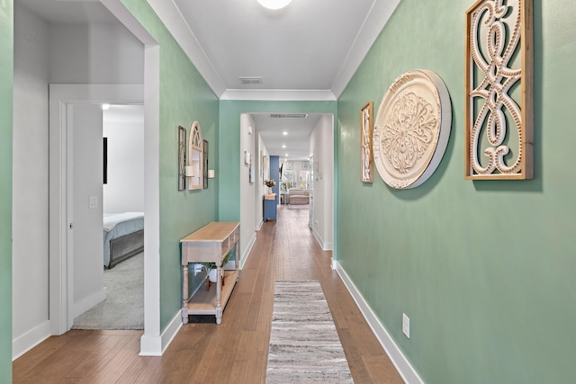 hall featuring visible vents, crown molding, baseboards, and wood finished floors