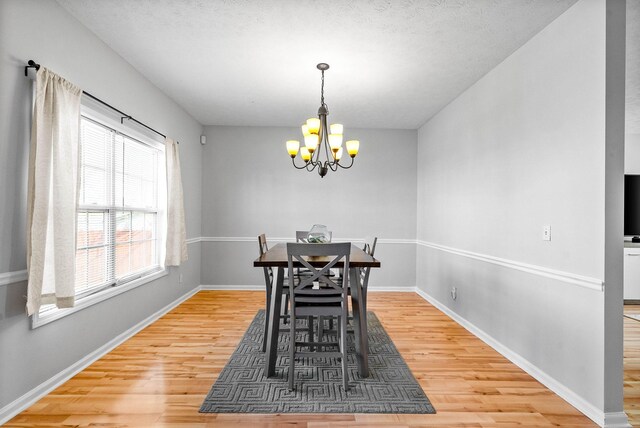 dining space with a chandelier, a textured ceiling, baseboards, and wood finished floors