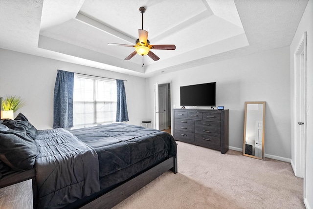 bedroom featuring light carpet, baseboards, a ceiling fan, a tray ceiling, and a textured ceiling