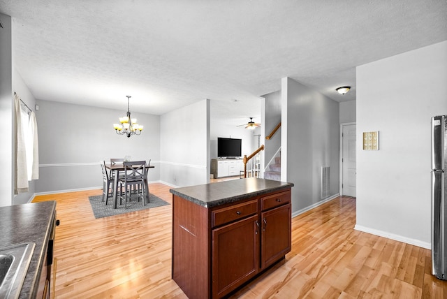 kitchen featuring light wood finished floors, dark countertops, open floor plan, freestanding refrigerator, and hanging light fixtures