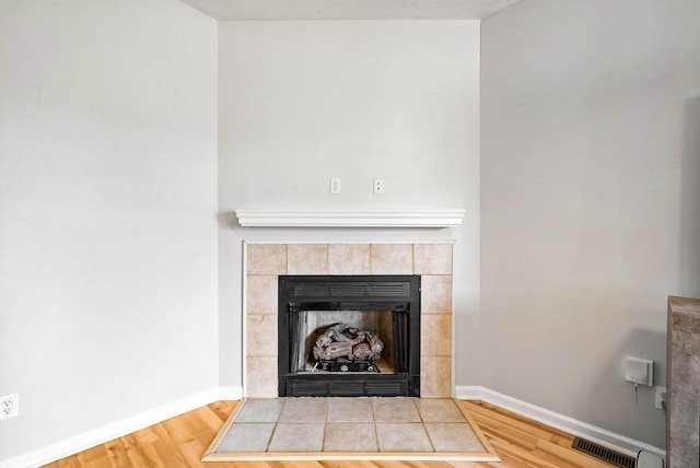 details featuring wood finished floors, a tile fireplace, visible vents, and baseboards