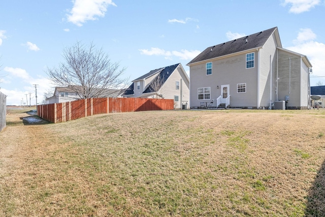 rear view of house featuring entry steps, central AC, a yard, and fence