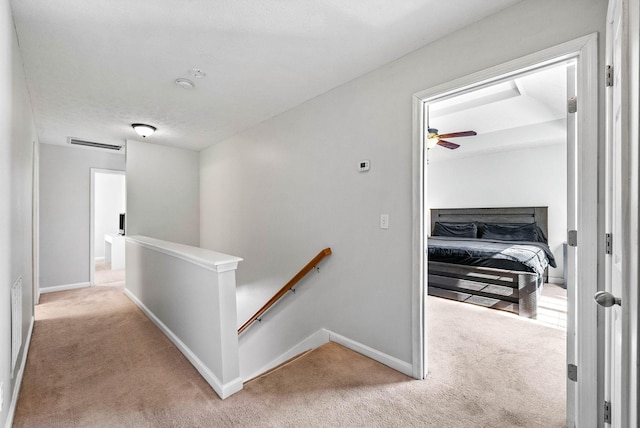 corridor with baseboards, visible vents, light colored carpet, and an upstairs landing