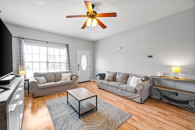 living area with ceiling fan, a textured ceiling, and wood finished floors