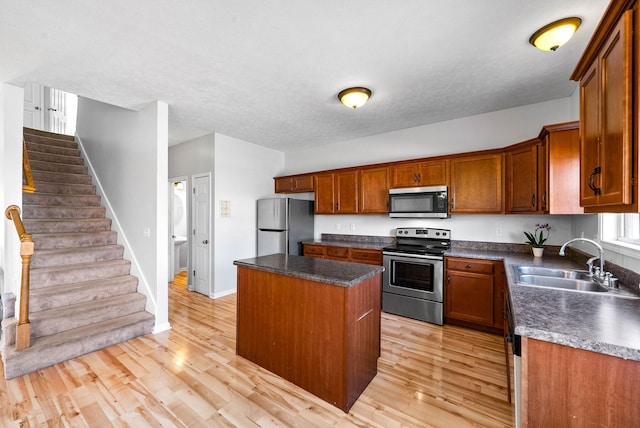 kitchen with stainless steel appliances, a sink, light wood-type flooring, a center island, and dark countertops