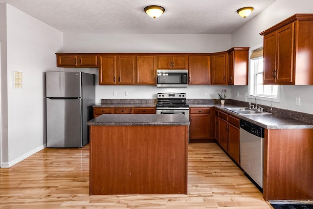 kitchen featuring a center island, light wood finished floors, dark countertops, appliances with stainless steel finishes, and a sink