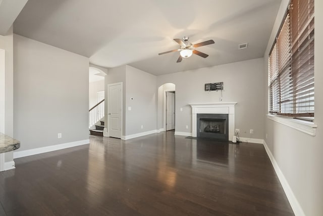 unfurnished living room with visible vents, baseboards, a ceiling fan, a fireplace with flush hearth, and dark wood-style flooring