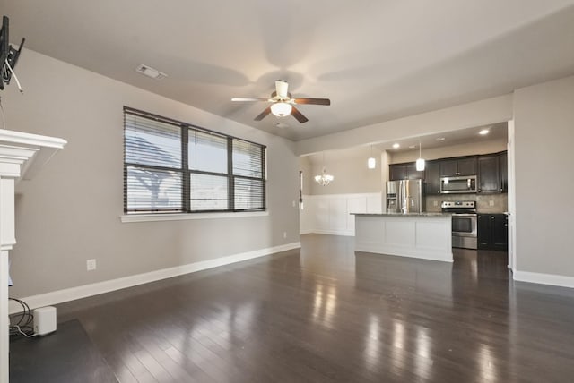 unfurnished living room featuring ceiling fan with notable chandelier, dark wood-style flooring, visible vents, and baseboards