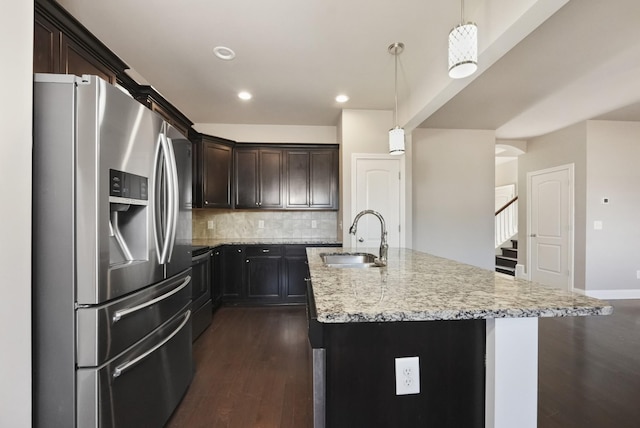 kitchen with light stone counters, pendant lighting, a center island with sink, stainless steel refrigerator with ice dispenser, and a sink