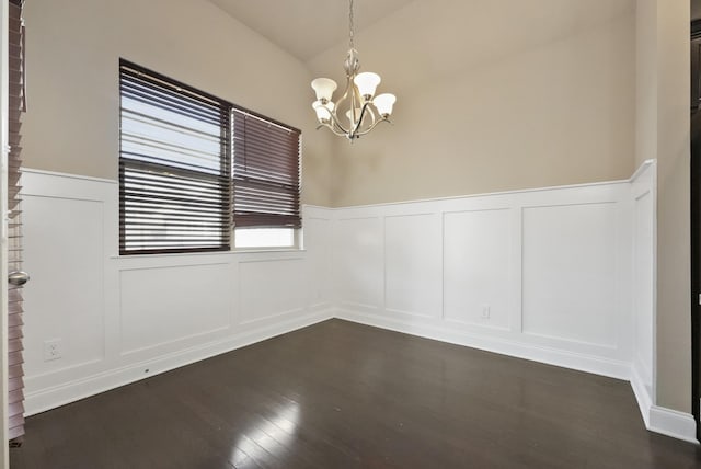 spare room with a wainscoted wall, lofted ceiling, a decorative wall, an inviting chandelier, and dark wood-type flooring