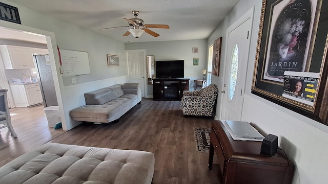 living room with wainscoting, wood finished floors, a ceiling fan, and a healthy amount of sunlight