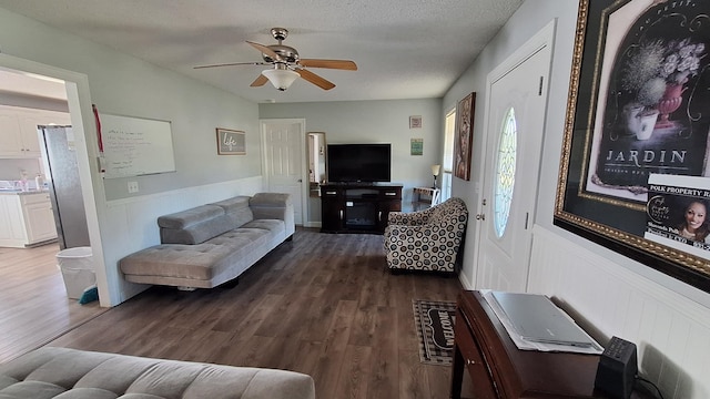 living area featuring a wainscoted wall, a textured ceiling, a ceiling fan, and dark wood-type flooring