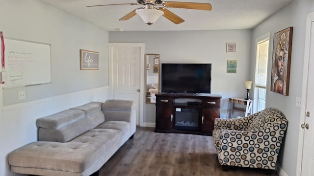 living area with a wainscoted wall, a ceiling fan, dark wood-type flooring, and a textured ceiling