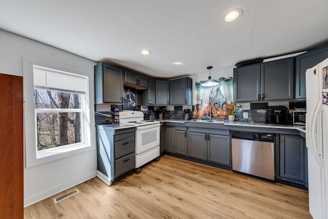 kitchen with light wood-type flooring, visible vents, gray cabinetry, a sink, and white appliances