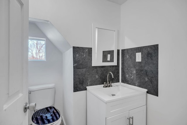 half bathroom featuring vanity, vaulted ceiling, toilet, and tile walls