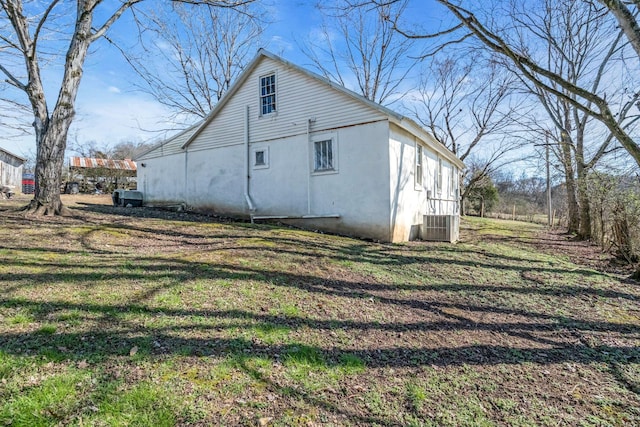 view of side of home featuring central air condition unit, stucco siding, and a yard