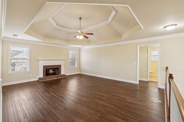 unfurnished living room with dark wood-style floors, a tray ceiling, ornamental molding, and a healthy amount of sunlight