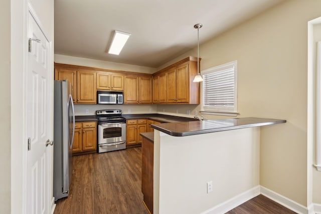 kitchen with stainless steel appliances, dark countertops, pendant lighting, and a peninsula