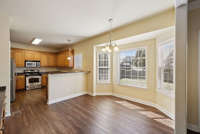 kitchen with pendant lighting, dark wood-style flooring, dark countertops, appliances with stainless steel finishes, and brown cabinetry