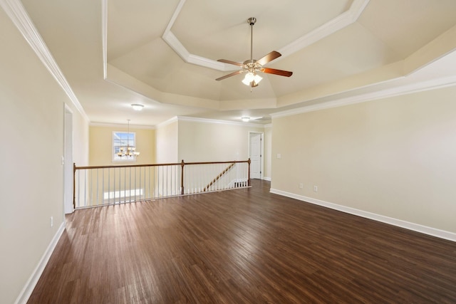 empty room featuring dark wood-style floors, a tray ceiling, crown molding, and baseboards