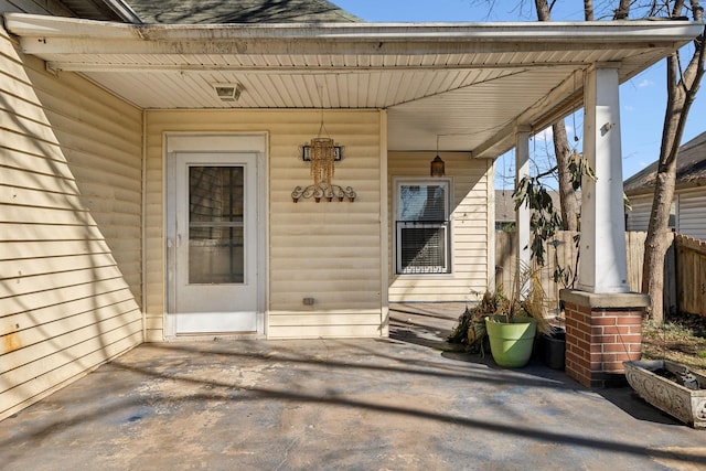 view of exterior entry with a shingled roof and fence