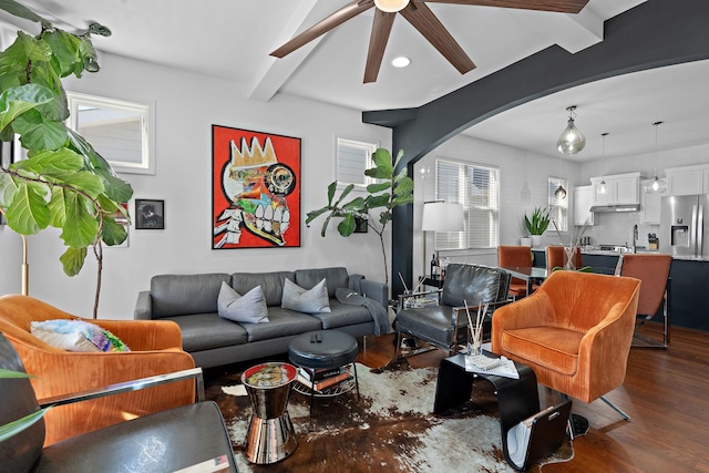 living area with plenty of natural light, arched walkways, beamed ceiling, and dark wood-style floors