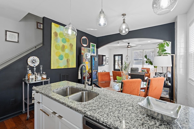 kitchen featuring arched walkways, a sink, white cabinetry, a ceiling fan, and dark wood finished floors