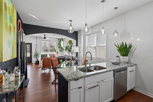 kitchen featuring arched walkways, stainless steel dishwasher, dark wood-style flooring, and a sink