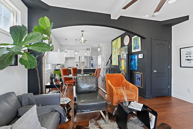 living area featuring baseboards, arched walkways, dark wood finished floors, and beam ceiling