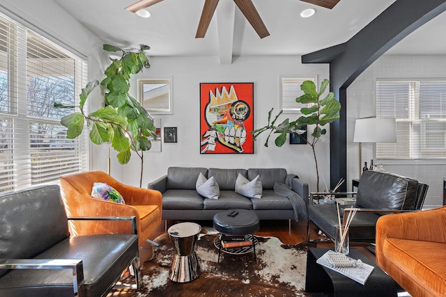 living area with arched walkways, wood finished floors, and beam ceiling