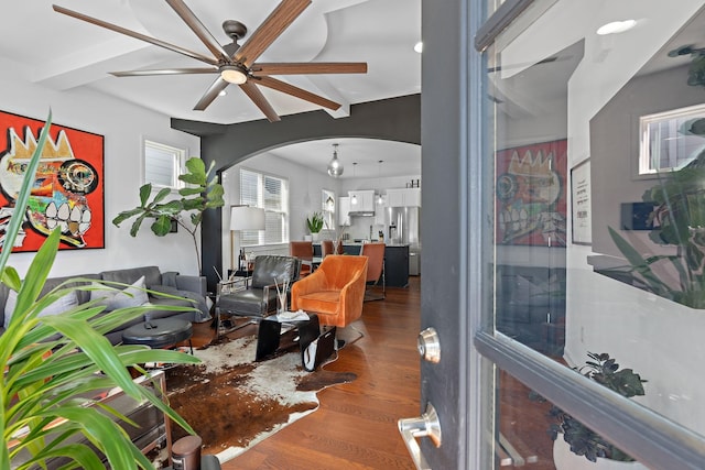 living area featuring a ceiling fan, arched walkways, beamed ceiling, and wood finished floors