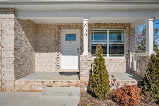 entrance to property featuring covered porch and brick siding