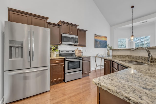 kitchen with light wood-style flooring, appliances with stainless steel finishes, decorative light fixtures, light stone countertops, and a sink