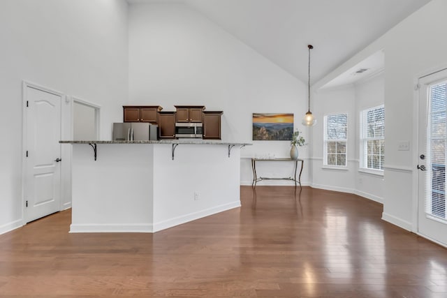 kitchen featuring stainless steel appliances, dark stone countertops, dark wood-type flooring, and a kitchen breakfast bar