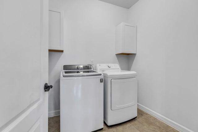 clothes washing area with cabinet space, light tile patterned floors, baseboards, and washer and dryer