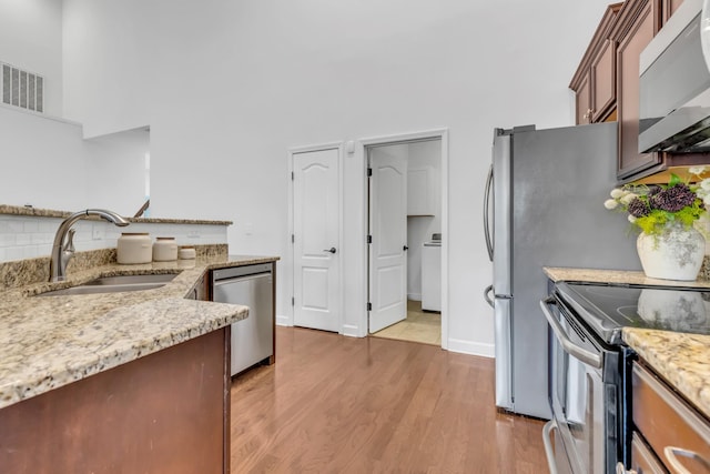 kitchen featuring visible vents, appliances with stainless steel finishes, light stone countertops, light wood-type flooring, and a sink