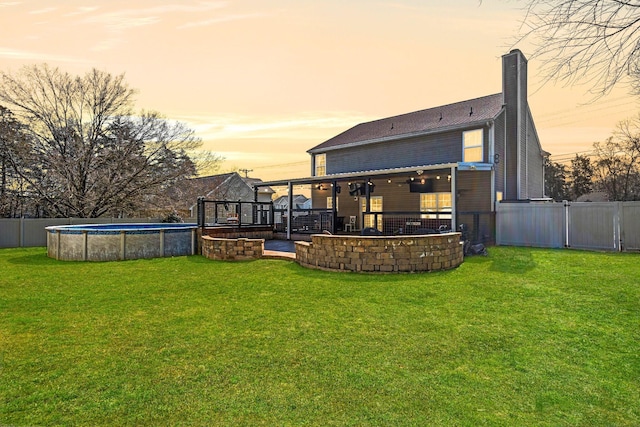 rear view of property featuring a yard, a chimney, a fenced backyard, and a fenced in pool