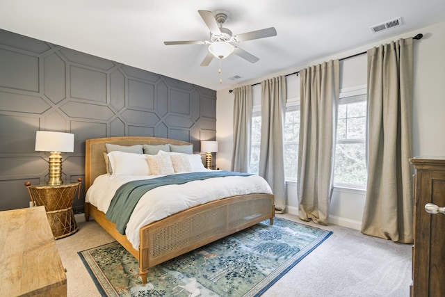 bedroom with ceiling fan, light colored carpet, an accent wall, visible vents, and baseboards