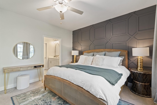 bedroom with light colored carpet, an accent wall, a ceiling fan, ensuite bath, and baseboards