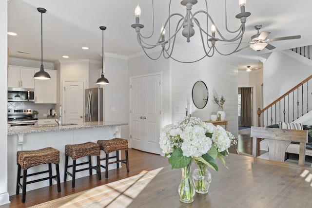 dining space with dark wood-style flooring, crown molding, recessed lighting, stairway, and ceiling fan with notable chandelier