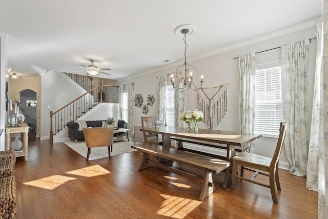 dining room with arched walkways, wood finished floors, crown molding, and stairs