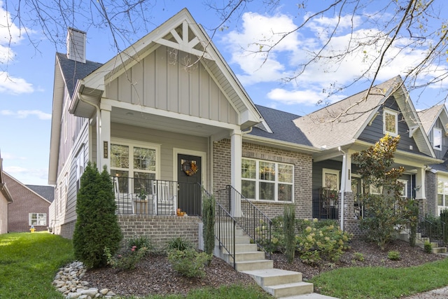 craftsman house featuring a porch, brick siding, a shingled roof, board and batten siding, and a chimney