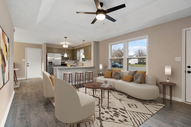 living room featuring a raised ceiling, a textured ceiling, baseboards, and wood finished floors