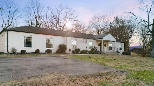 ranch-style house with covered porch, a yard, and brick siding