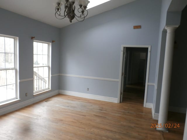 spare room with visible vents, a notable chandelier, baseboards, and wood finished floors