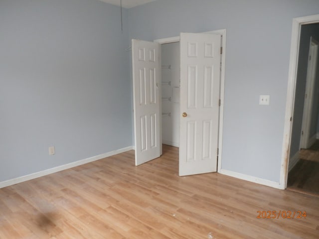 unfurnished bedroom featuring a closet, light wood-style flooring, baseboards, and a spacious closet