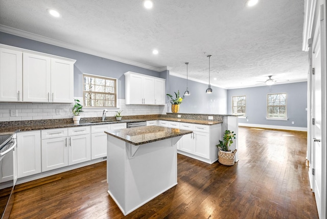 kitchen featuring a sink, white cabinetry, open floor plan, dark stone counters, and decorative light fixtures