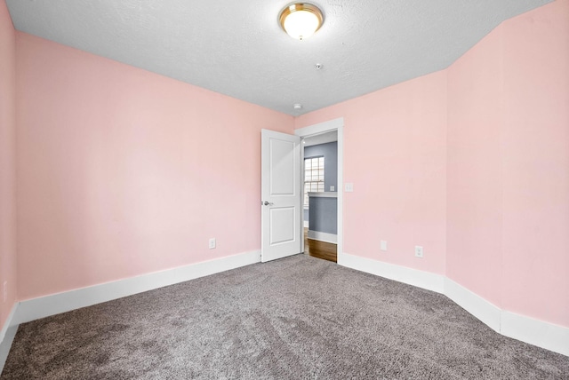 carpeted spare room featuring a textured ceiling and baseboards