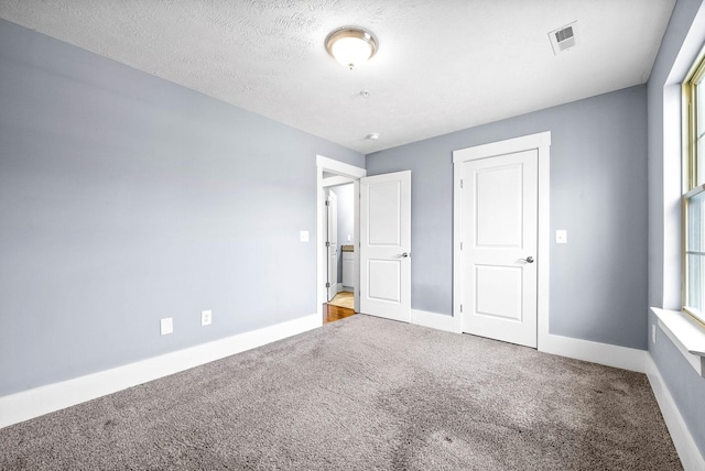 unfurnished bedroom featuring a textured ceiling, carpet, visible vents, and baseboards